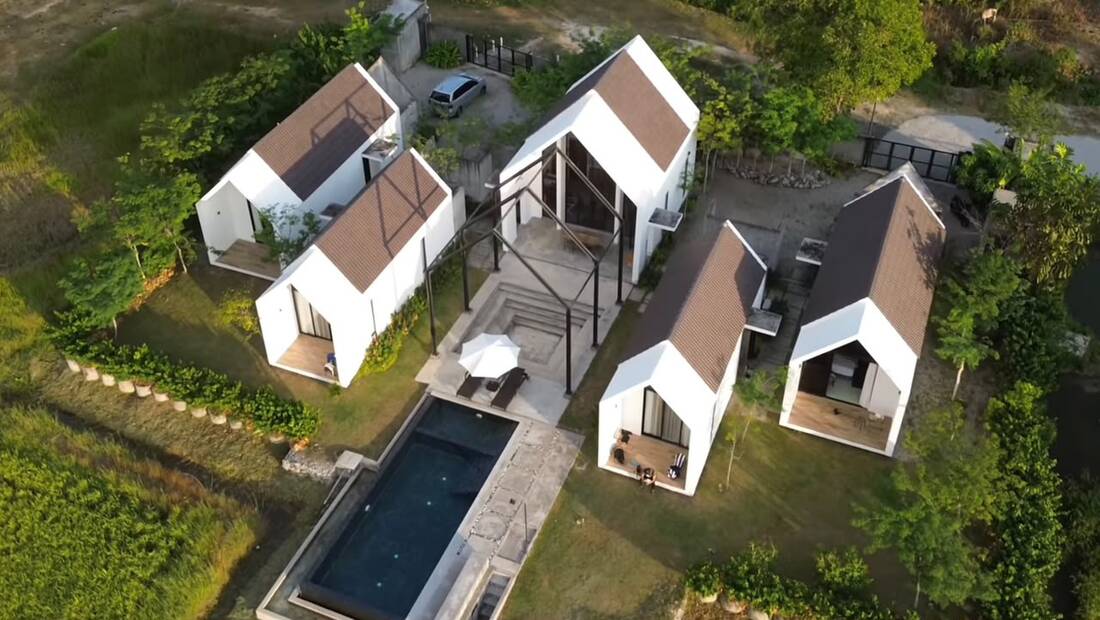 Aerial view of Ezu Isle: four A-frame suites and the central glass hall arranged around the pool, padi fields on both sides