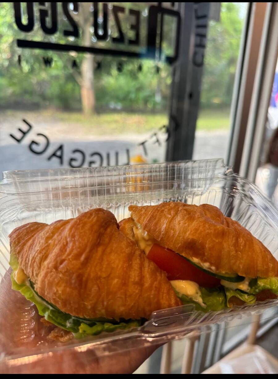 Croissant sandwiches with lettuce, tomato and cucumber in a takeaway box, held up at the shopfront
