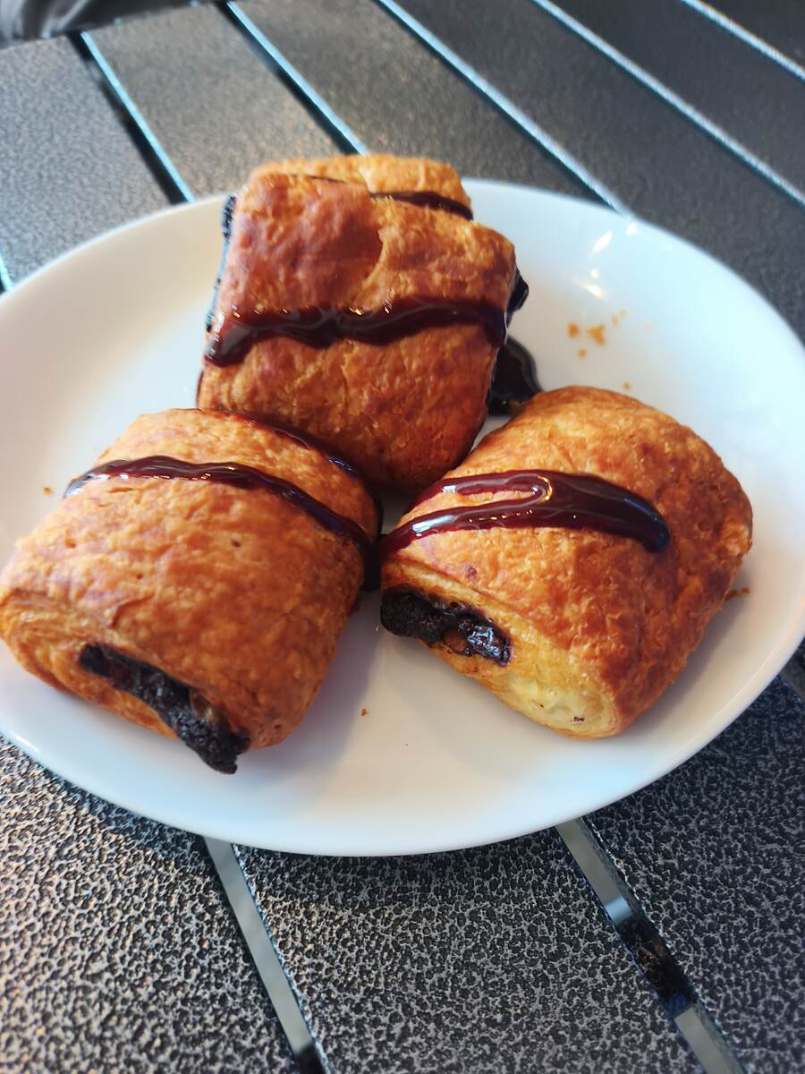 Three flaky pain au chocolat with dark chocolate drizzle on a plate